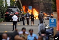 Security forces help civilians flee the scene as cars burn behind, at a hotel complex in Nairobi, Kenya, Jan. 15, 2019.