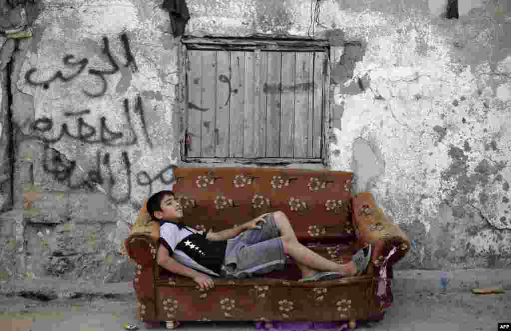 A Palestinian boy rests on an old armchair in front of a dilapidated house in Gaza City.