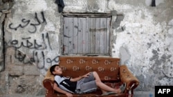 A Palestinian boy rests on an old armchair in front of a dilapidated house on May 22, 2015 in Gaza City.