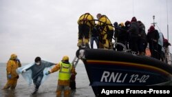 Para migran tampak dibantu oleh anggota Institut Nasional Kapal Penyelat Inggris (RNLI) setelah tiba di Dungeness, di bagian pesisir tenggara Inggris, pada 24 November 2021. Para migran itu diselamatkan dalam perjalanan mereka melewati Selat Inggris. (Foto: AFP/Ben Stansall)