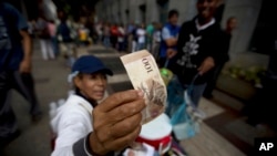 A street vendor inspects the authenticity of a 100-bolivar note as people stand in line outside a bank to deposit their 100-bolivar bank notes in Caracas, Venezuela, Dec. 13, 2016.