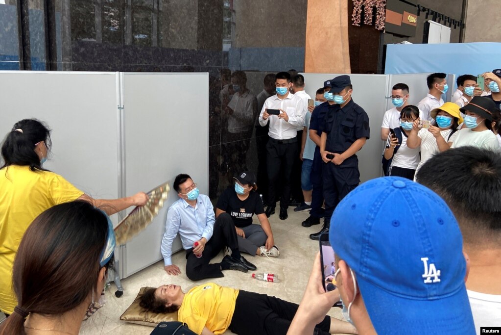 与要求兑付逾期理财产品的抗议群众现场对话的恒大财富执行董事兼总经理杜亮坐在一名躺倒在地需要救助的妇女旁。（2021年9月13日）(photo:VOA)