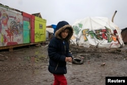 Aida, a nine-year-old Kurdish girl, walks in the mud in the southern part of a camp for migrants called the "jungle" during a rainy winter day in Calais, northern France, Feb. 22, 2016.