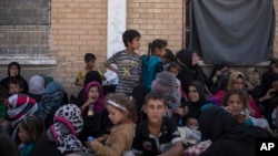 FILE - Women and children from Hawija sit outside a Kurdish screening center to determine if they were associated with the Islamic State group, in Dibis, Iraq, Oct. 3, 2017.