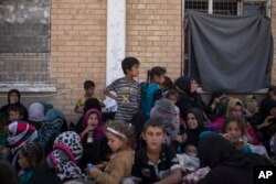 FILE - Women and children from Hawija sit outside a Kurdish screening center to determine if they were associated with the Islamic State group, in Dibis, Iraq, Oct. 3, 2017.