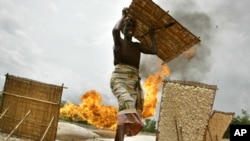 An unidentified woman carries her tapioca after drying it near a gas flare belonging to the Shell oil company in Utorogun, Nigeria, March 5, 2006 (file photo).
