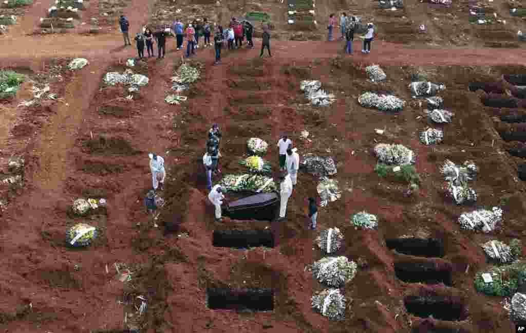 Cemetery workers wearing protective gear lower the coffin of a person who died from complications related to COVID-19 into a gravesite at the Vila Formosa cemetery in Sao Paulo, Brazil, April 7, 2021.