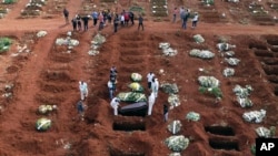 FILE - In this April 7, 2021, file photo, cemetery workers wearing protective gear lower the coffin of a person who died from complications related to COVID-19 into a gravesite at the Vila Formosa cemetery in Sao Paulo, Brazil. 