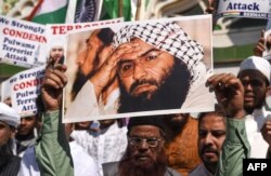 FILE - Indian Muslims hold a scratched photo of Jaish-e-Mohammad group chief, Maulana Masood Azhar, as they shout slogans against Pakistan during a protest in Mumbai, Feb. 15, 2019.