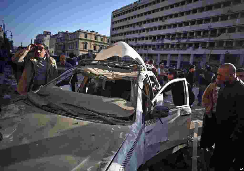 Pessoas olham para um taxi destruído após explosão na sede da polícia, na baixa do Cairo, Jan. 24, 2014.