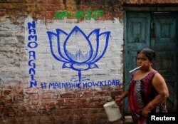 FILE - A woman walks past a wall painted with the election symbol of India's ruling Bharatiya Janata Party (BJP) in an alley at a residential area in Kolkata, India, March 22, 2019.