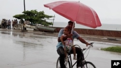 A man balances a child and umbrella on his bike as it rains during the approach of Hurricane Sandy in Manzanillo, Cuba, Oct. 24, 2012.