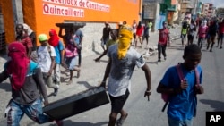 13일 아이티 수도 포르토프랭스에서 반정부 시위가 계속된 가운데, 복면을 쓴 남성들이 주변 상점에서 훔친 TV를 들고 있다.