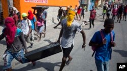 Masked looters carry a flat screen TV amid protests demanding the resignation of Haitian President Jovenel Moise near the presidential palace in Port-au-Prince, Haiti, Feb. 13, 2019. 