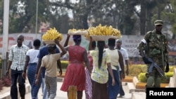 FILE - Women carry baskets of banana as they walk past a military personnel patrolling in Uganda's capital Kampala, February 19, 2016. 