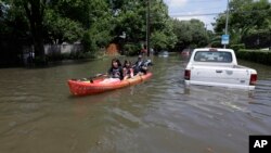 Residentes en Houston, Texas, se desplazan en una embarcación en una calle inundada por las torrenciales lluvias.