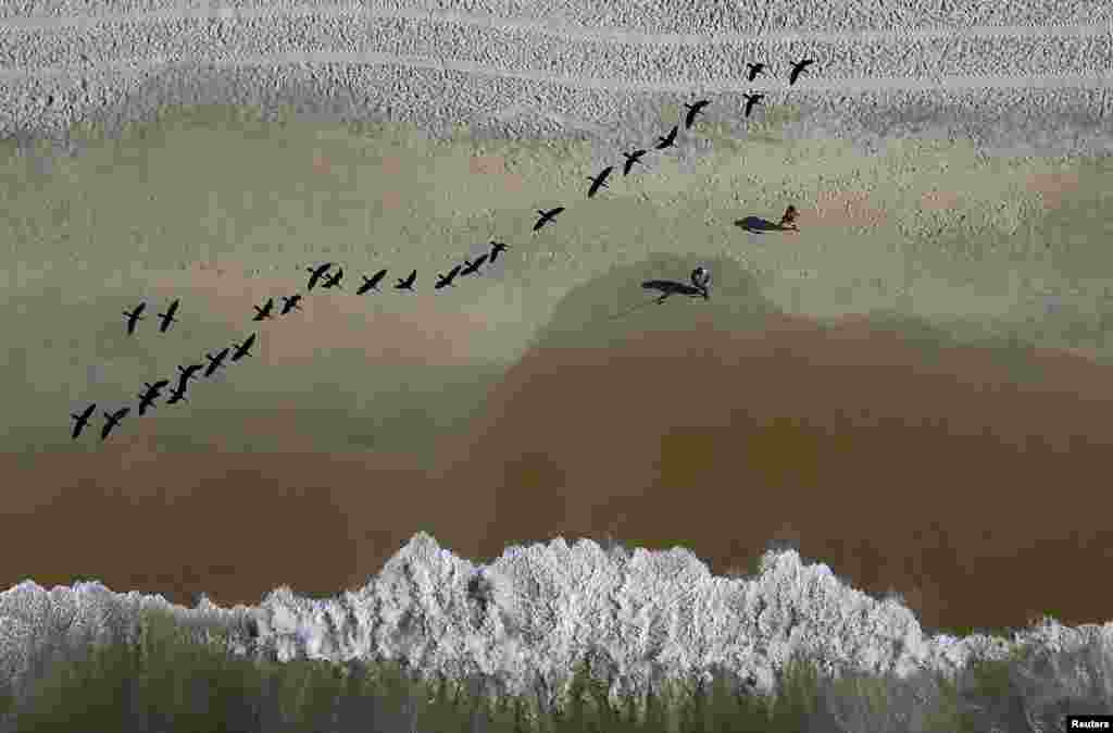 A fisherman casts his line as birds fly over the Sao Conrado beach in Rio de Janeiro, Brazil.