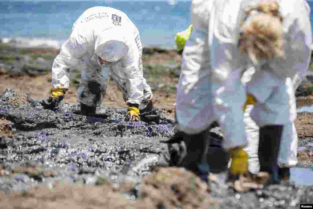 Volunteers collect fuel oil from rocks at the &quot;Muelle Viejo&quot; beach in Gran Canaria in Spain&#39;s Canary Islands. A Russian ship, carrying 1,409 tons of fuel oil, caught fire in Las Palmas port and authorities towed it out to sea where it sank offshore April 14 around 15 nautical miles south of Gran Canaria. The Development Ministry says they continue to take protective measures to avoid slicks spotted off beaches in the area.