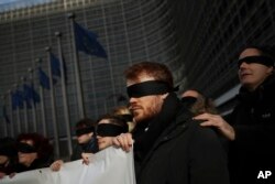Blindfolded protesters against Brexit hold a banner outside the European Commission headquarters during a meeting between European Commission President Jean-Claude Juncker and British Prime Minister Theresa May in Brussels, Feb. 7, 2019.