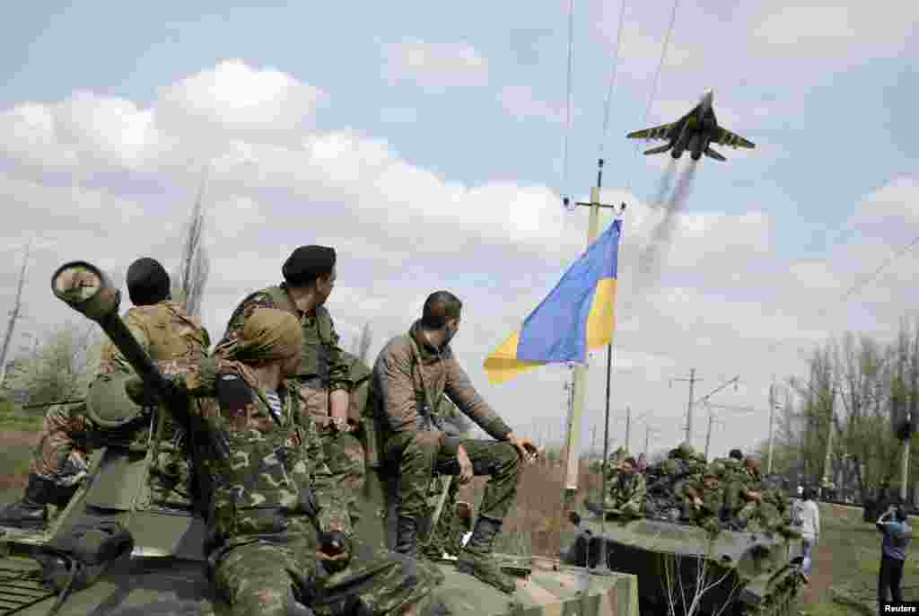 Ukrainian servicemen look at a Ukrainian military jet fly above them while they sit on top of armored personnel carriers in Kramatorsk, Ukraine, April 16, 2014. 
