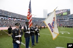 FILE - Members of the U.S. Army color guard join color guards from other military services for the National Anthem before an NFL football game between the Atlanta Falcons and Carolina Panthers in Charlotte, North Carolina, Nov. 16, 2014.