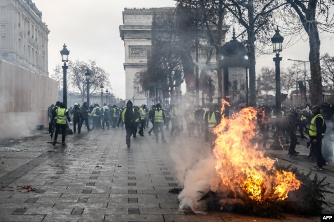 Protesters wearing yellow vests stand next to a burning tree as they demonstrate against the rising costs of living that they blame on high taxes near the Arc de Triomphe on the Champs-Elysees avenue in Paris, Dec. 8, 2018.