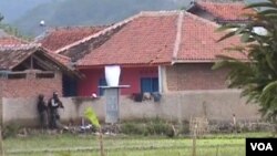 Dua petugas Densus 88 sedang mengintai rumah bercat merah (kanan) yang di dalamnya berisi empat tersangka teroris (foto: Wulan/VOA).