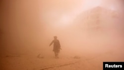 FILE - A rebel fighter runs through dust towards an area damaged by what activists said were barrel bombs dropped by warplanes loyal to Syria's President Bashar al-Assad in Aleppo, Nov. 6, 2014. 