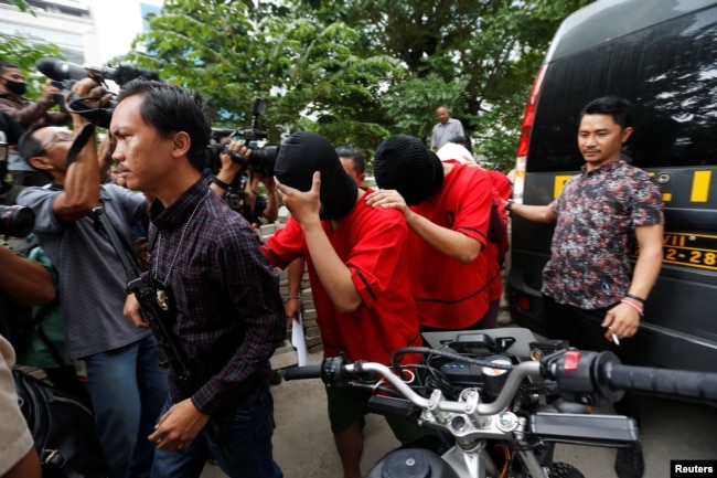 FILE - A plainclothes policeman holds a rifle as he escorts suspects during a police investigation into a men's club after a weekend raid on what authorities described as a "gay spa" in Jakarta, Indonesia, Oct. 9, 2017.