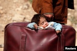 FILE - A child sleeps in a bag in the village of Beit Sawa, eastern Ghouta, Syria, March 15, 2018.