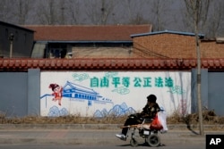 A Chinese woman in an electric wheelchair motors past traditional government propaganda, with the Chinese words "Freedom, Equality, Fairness, Rule by Law," on the outskirts of Beijing, March 2, 2016.