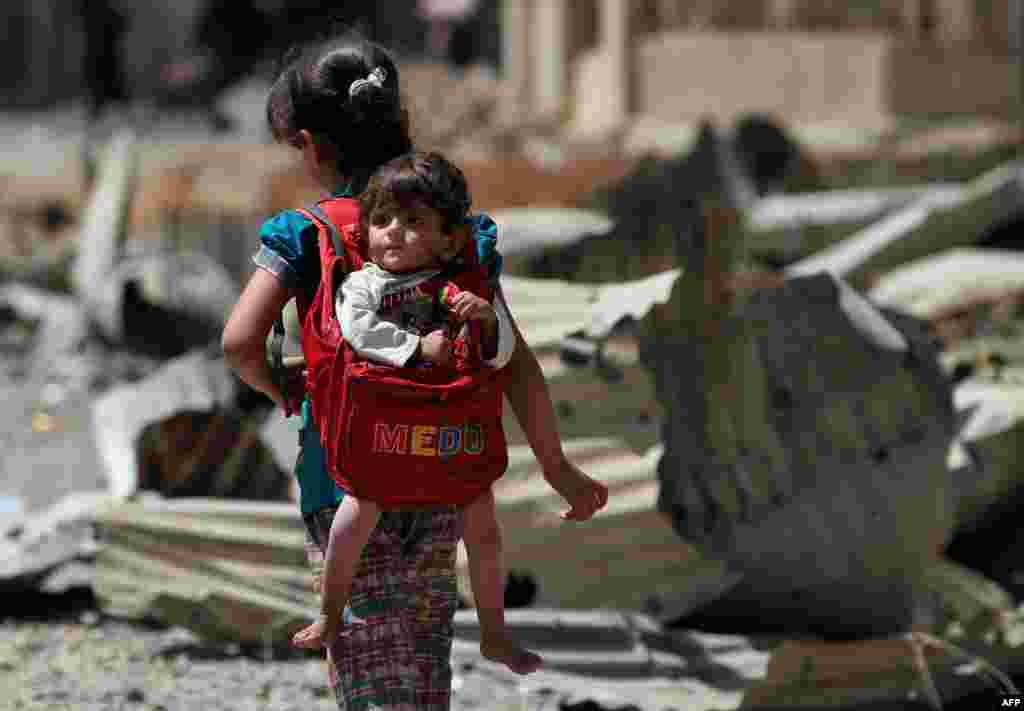 An Iraqi girl carries a baby in a backpack turned into a baby carrier as displaced Iraqis from western Mosul&#39;s al-Islah al-Zaraye neighborhood flee their area, during a government forces&#39; military offensive to retake the area from Islamic State (IS) group fighters.