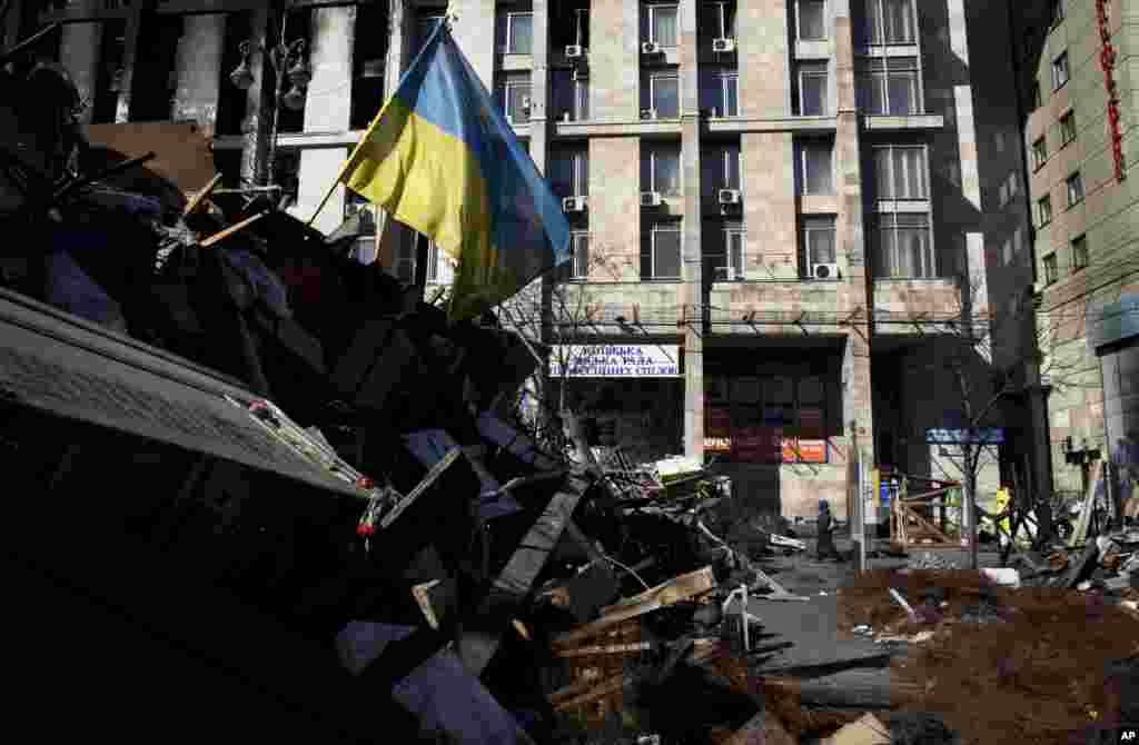 A woman walks past a barricade as a Ukrainian flag flutters in the wind in Kyiv's Independence Square, March 13, 2014.