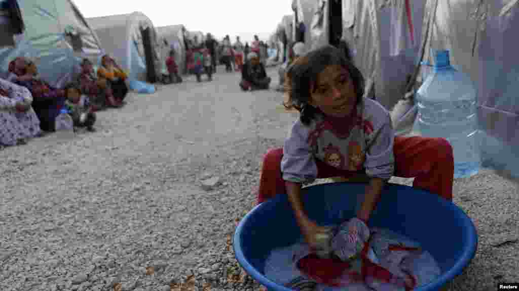 A Kurdish refugee girl from the Syrian town of Kobani washes in front of their family tent in a camp near the Syria-Turkey border in the southeastern town of Suruc, Turkey, Oct. 10, 2014. 