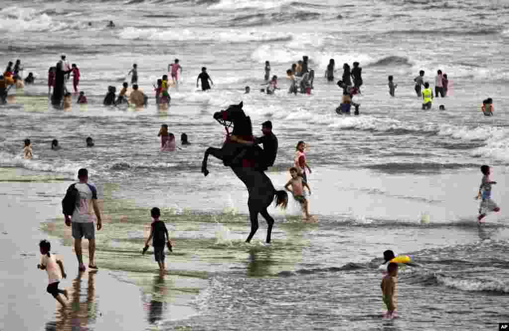 A man rides a horse while others swim on the beach of Gaza City.