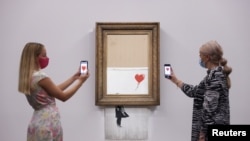 A gallery assistant poses by 'Love is in the Bin', an artwork by Banksy, which will be for sale in an auction, at Sotheby's in London, Britain, September 3, 2021. 