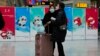 Passengers wearing masks to protect them from the coronavirus stand near Beijing Winter Olympics posters at the South Train Station in Beijing, Jan. 14, 2022.