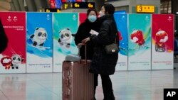 Passengers wearing masks to protect them from the coronavirus stand near Beijing Winter Olympics posters at the South Train Station in Beijing, Jan. 14, 2022.