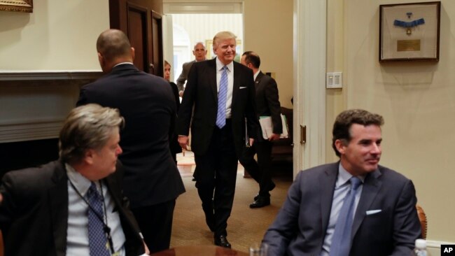 President Donald Trump smiles as he walks in from the Oval Office of the White House in Washington, Monday, Jan. 23, 2017, to host breakfast with business leaders in the Roosevelt Room. Sitting at the table are White House Senior Adviser Steve Bannon, left, and Kevin Plank, founder, CEO and Chairman of Under Armour. (AP Photo/Pablo Martinez Monsivais)