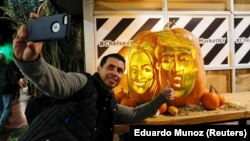 A man takes a selfie next to a giant pumpkin created by Master Carver Hugh McMahon with the faces of 2016 Democratic nominee Hillary Clinton and Republican presidential nominee Donald Trump at Chelsea Market in New York, U.S., October 28, 2016. 