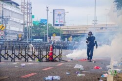FILE - A photographer in a gas mask walks away from a line of police while covering clashes between protesters and security in Bangkok, Thailand, Aug. 7, 2021.