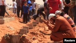 Men pray over a grave at the funerals for those killed in Saturday's clashes at the Libya Shield brigade headquarters, in Benghazi Jun. 9, 2013.