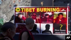Tibetan Buddhist nuns pass by a poster showing pictures of those who have self-immolated since March, Dharmsala, India, Oct. 19, 2011.