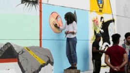 In this Sunday, Nov. 17, 2019 photo, an Iraqi artist woman draws graffiti at the Saadoun Tunnel, in Baghdad, Iraq. The tunnel that passes under Baghdad’s landmark Tahrir Square has become an ad hoc museum for Iraq's revolution: Young artists draw images a