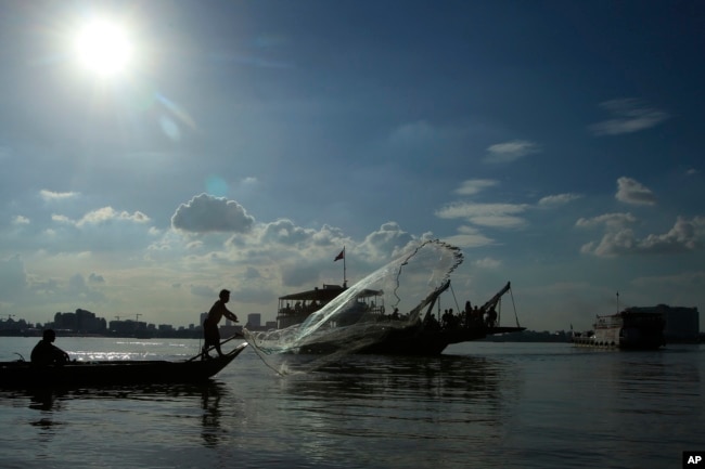 FILE - A fisherman casts his net next to a ferry in the Mekong River near Phnom Penh, Cambodia, Dec. 1, 2015.