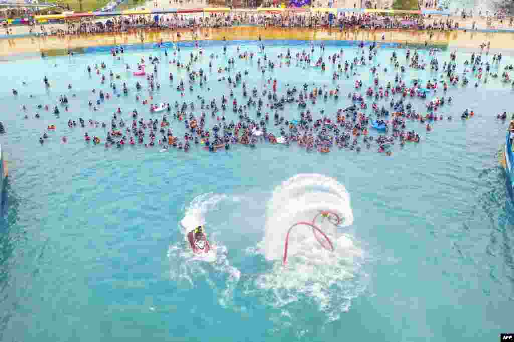 People watch a flyboard performance as they cool off in a swimming pool in Lianyungang, in China&#39;s eastern Jiangsu province, July 4, 2021.