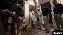 Police stand guard as a polio worker waits to give polio vaccine drops to children at a street in Peshawar, the capital of Khyber-Pakhtunkhwa province, Pakistan, March 30, 2014.