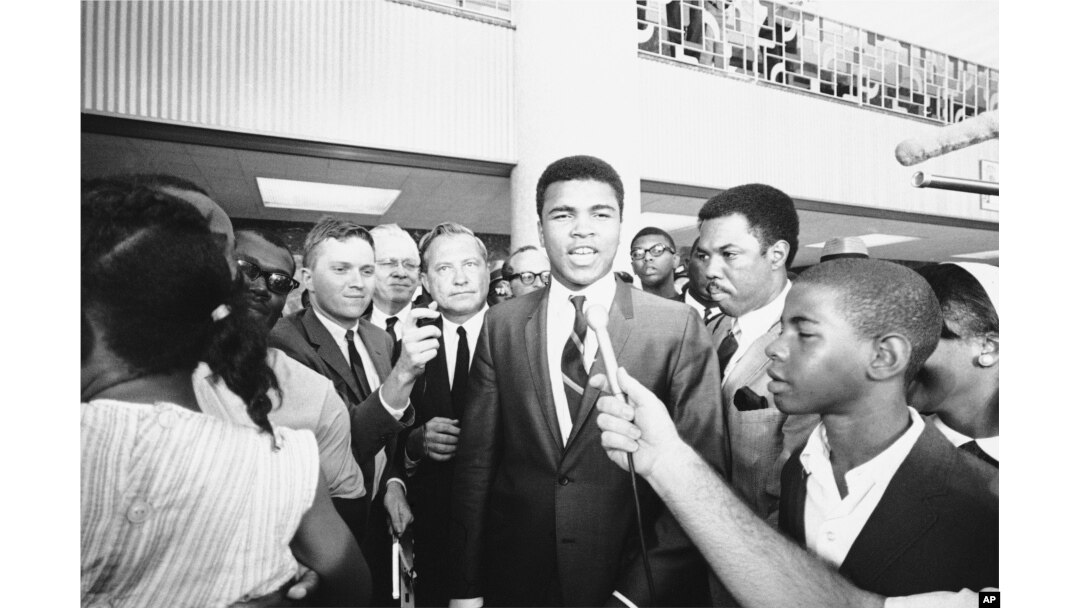 FILE - With one of his attorneys Quinnan Hodges (L) of Houston, looking on, Muhammad Ali speaks to the press, radio and television after an all-white jury found him guilty of refusing to be inducted.