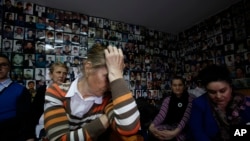 Bosnian Muslim woman who lost their family members in Srebrenica, Habiba Masic, Fatima Mujic, Vasvija Kadic and Mirsada Kahriman, from left to right, react as they watch a TV broadcast of the sentencing of Radovan Karadzic at the International Criminal Tribunal for Former Yugoslavia (ICTY) in The Hague, with photos of missing Bosnian people plastered on a walls at the union of Srebrenica mothers, in Tuzla, Bosnia, on Thursday, March, 24, 2016.