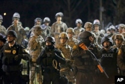 FILE - Police and Missouri National Guardsmen stand guard as protesters gather in front of the police department in Ferguson, Nov. 28, 2014.